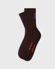 The Mercer Socks in brown are comfortable ribbed crew socks featuring a small star patch at the cuff and orange text near the toe.