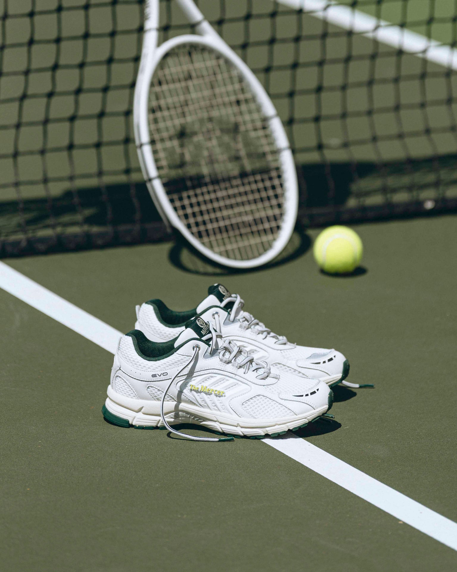 A pair of white Re-Run EVO sneakers are standing on a tennis court, viewed from the side.