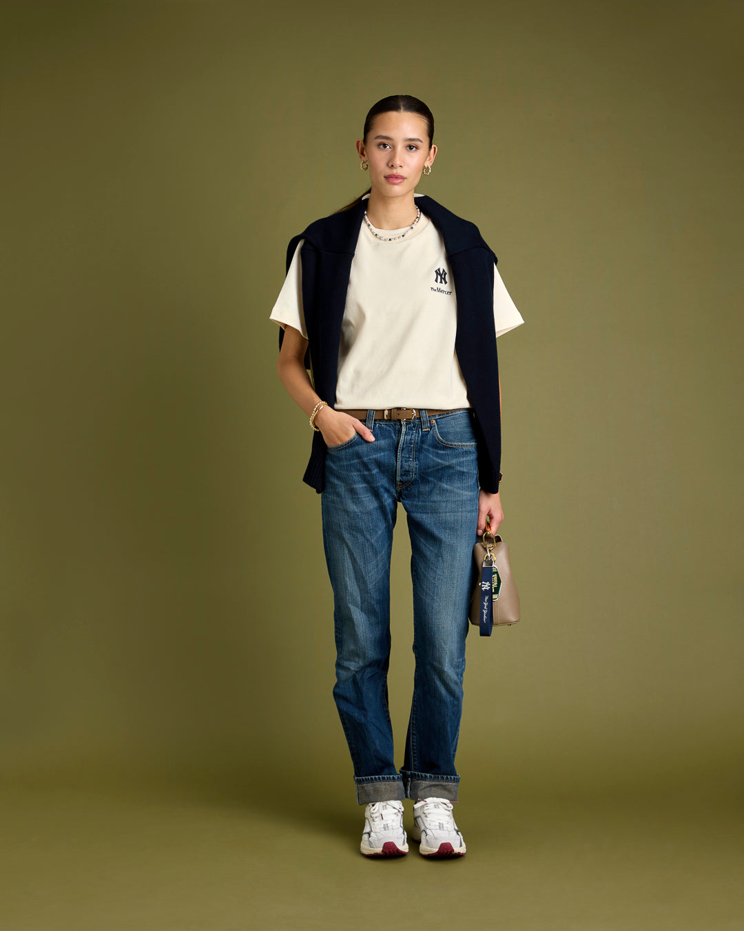 A woman is wearing The Mercer 47 Tee with New York Yankees in white paired with The Re-Run White/Silver in White/Red.