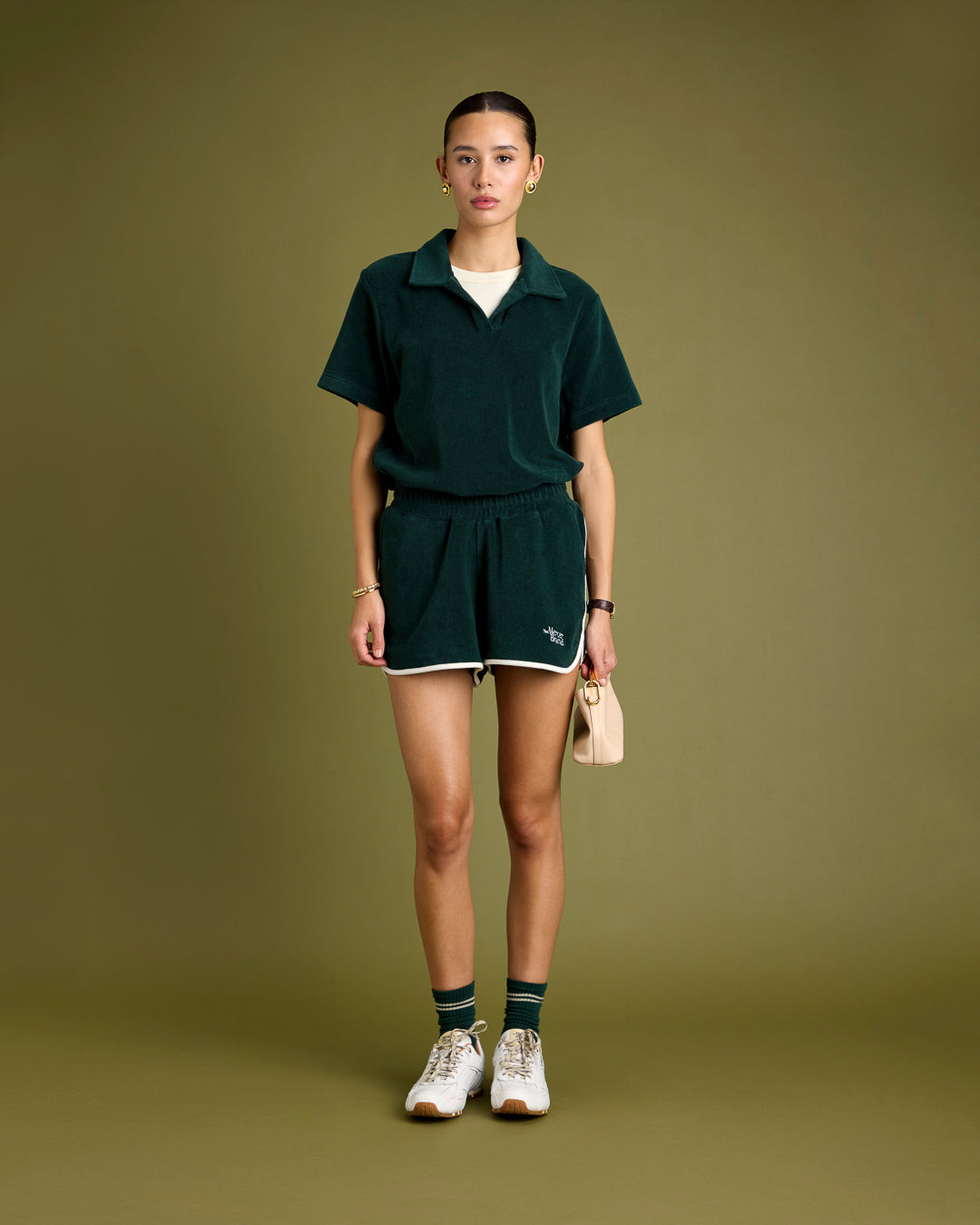 A woman is wearing a green terry toweling set consisting of a polo and matching shorts, paired with green tennis socks and finished with The Re-Run Drive sneakers. in white