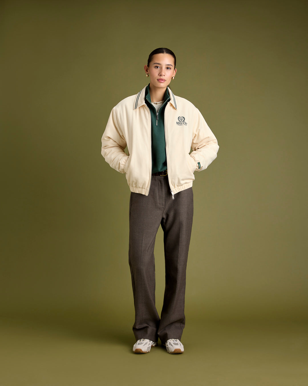 A woman is wearing The Mercer jacket with The Mercer Tennis quarter zip. The shoes she is wearing are The Re-Run Drive in off white.