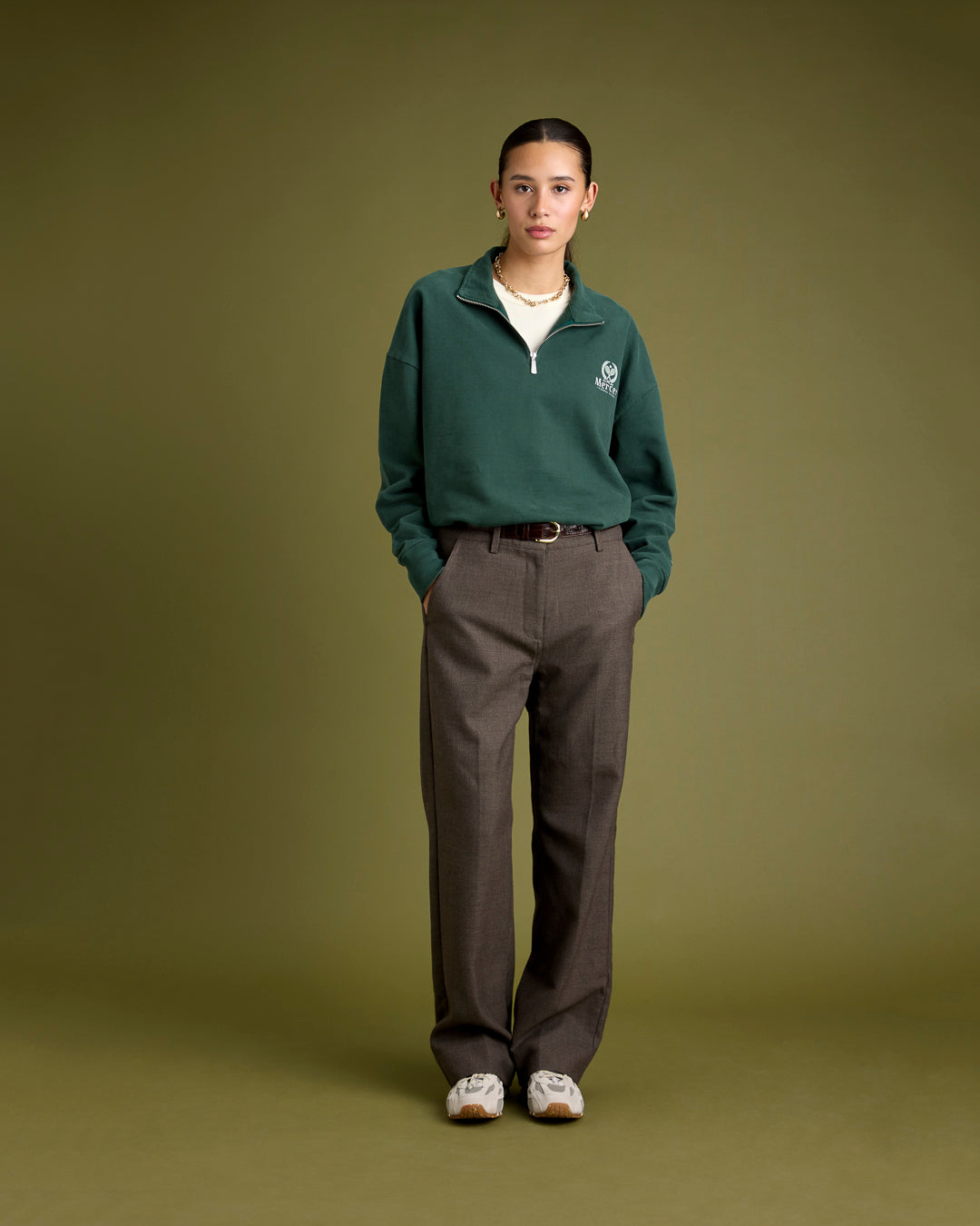 A woman is wearing The Mercer Tennis Quarter zip in green paired with The Re-Run Drive in off white.