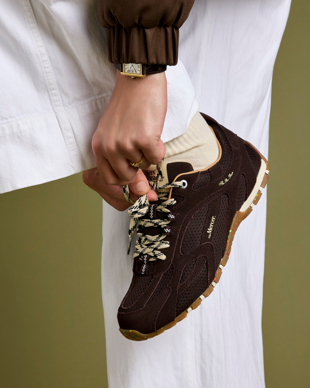 A woman ties the laces of her The Re-Run Drive in brown, paired with The Mercer socks in off white.