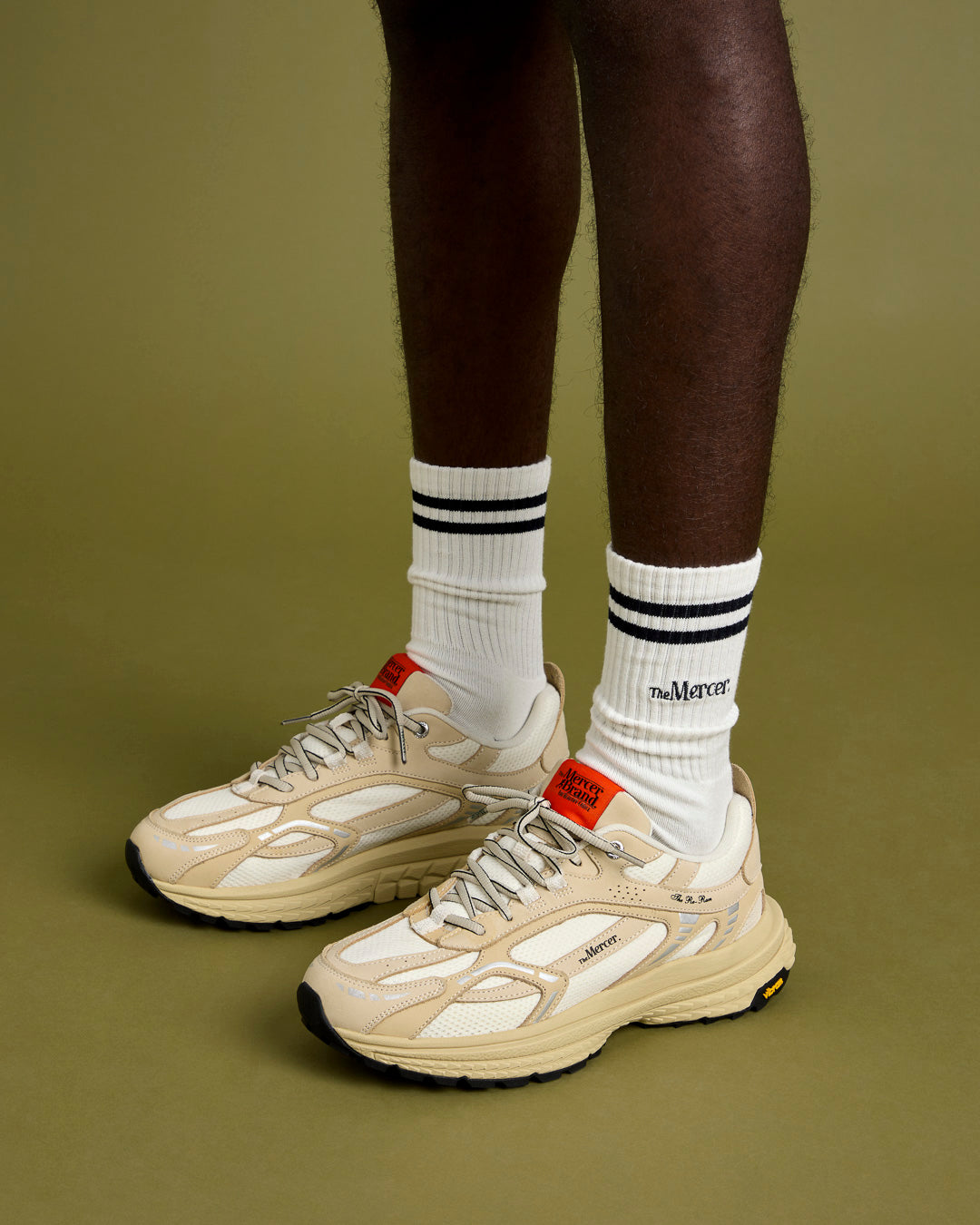 The Re-Run Vibram in Off White on foot shot on model with white the mercer brand sock and orange detail on the tongue of the shoe 
