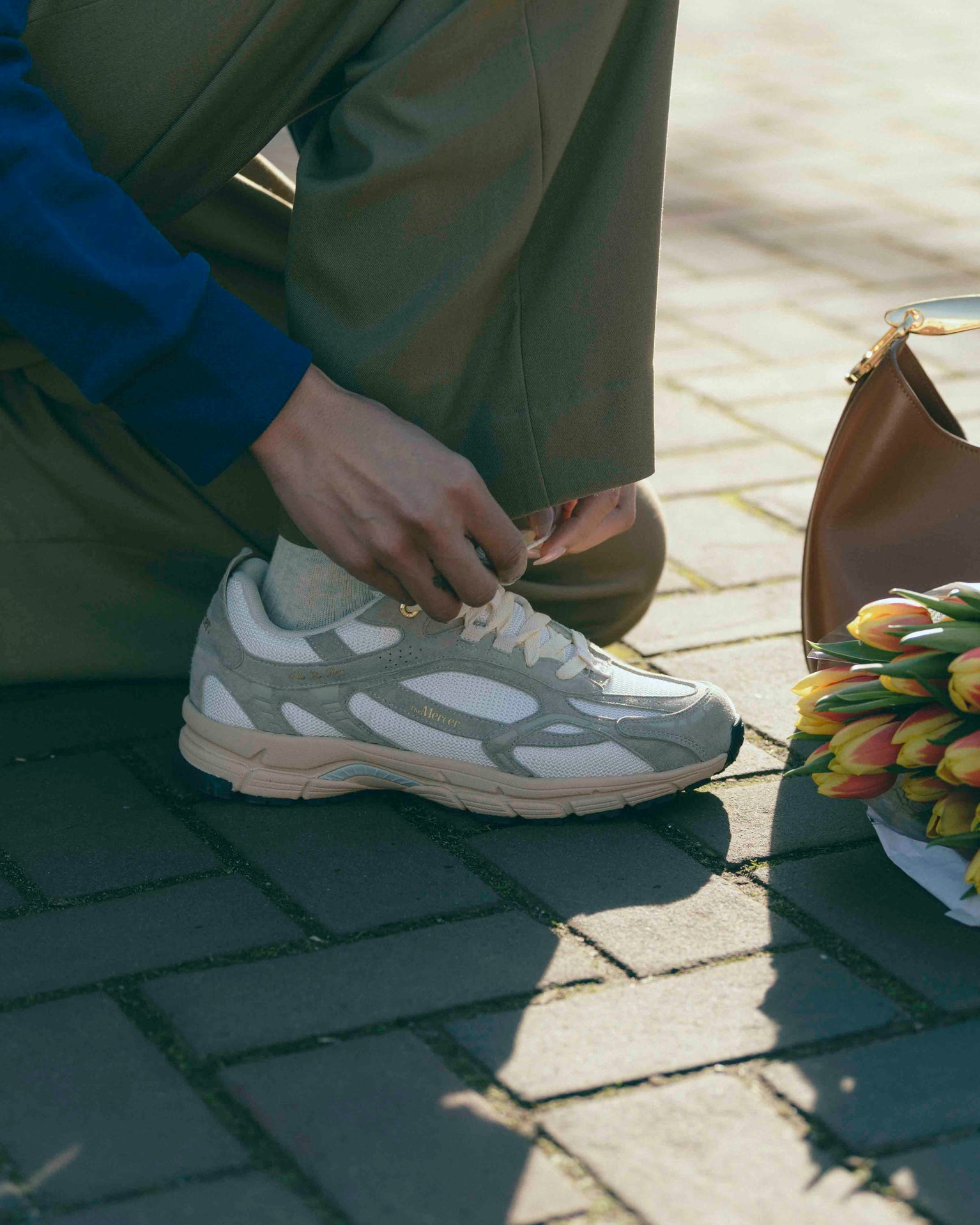 A woman is tying the laces of The Re-Run Desert in sand.