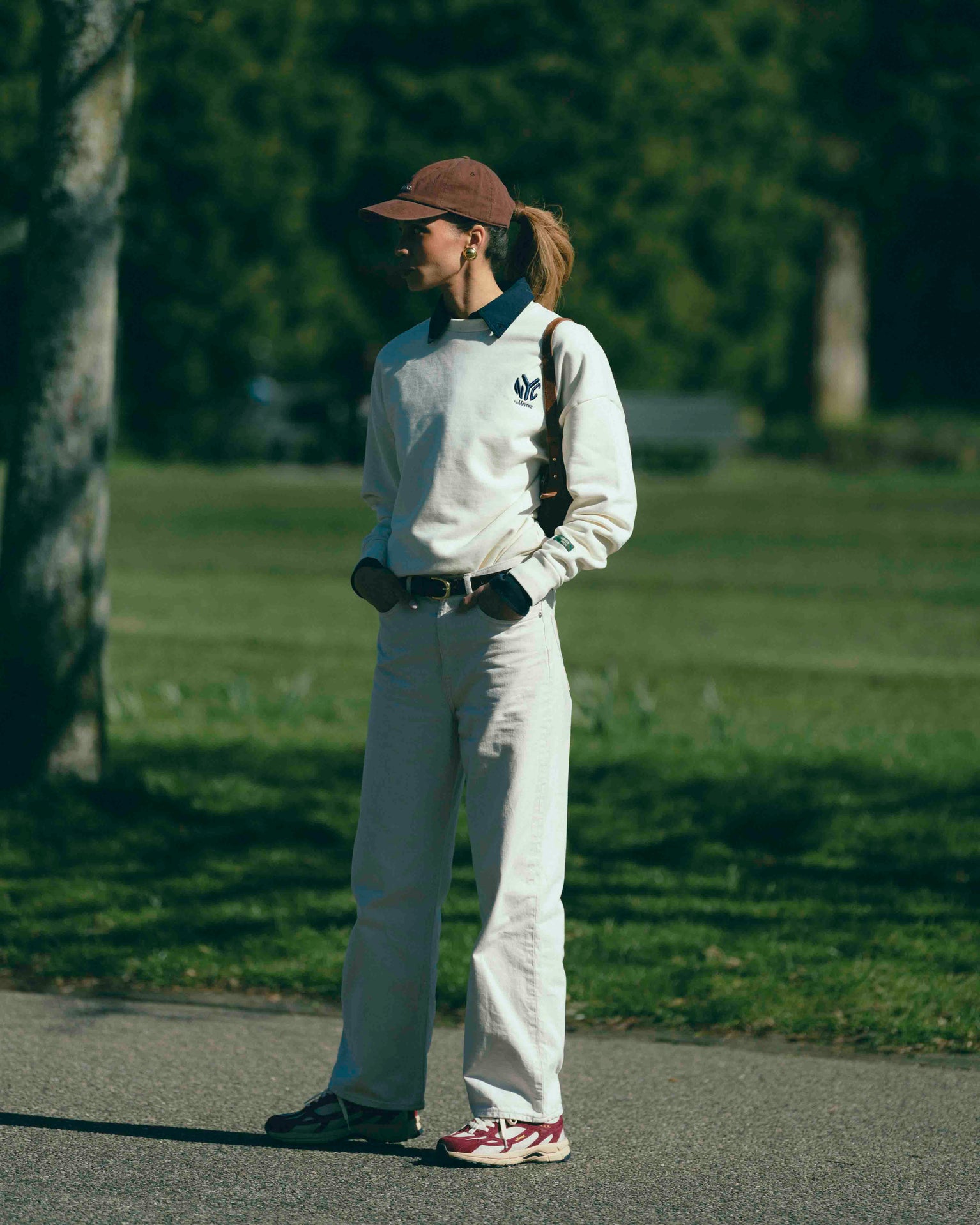 A woman is wearing The Subway Sweater and The Mercer Cap paired with The Re-Run desert 2.0 in bordeaux.