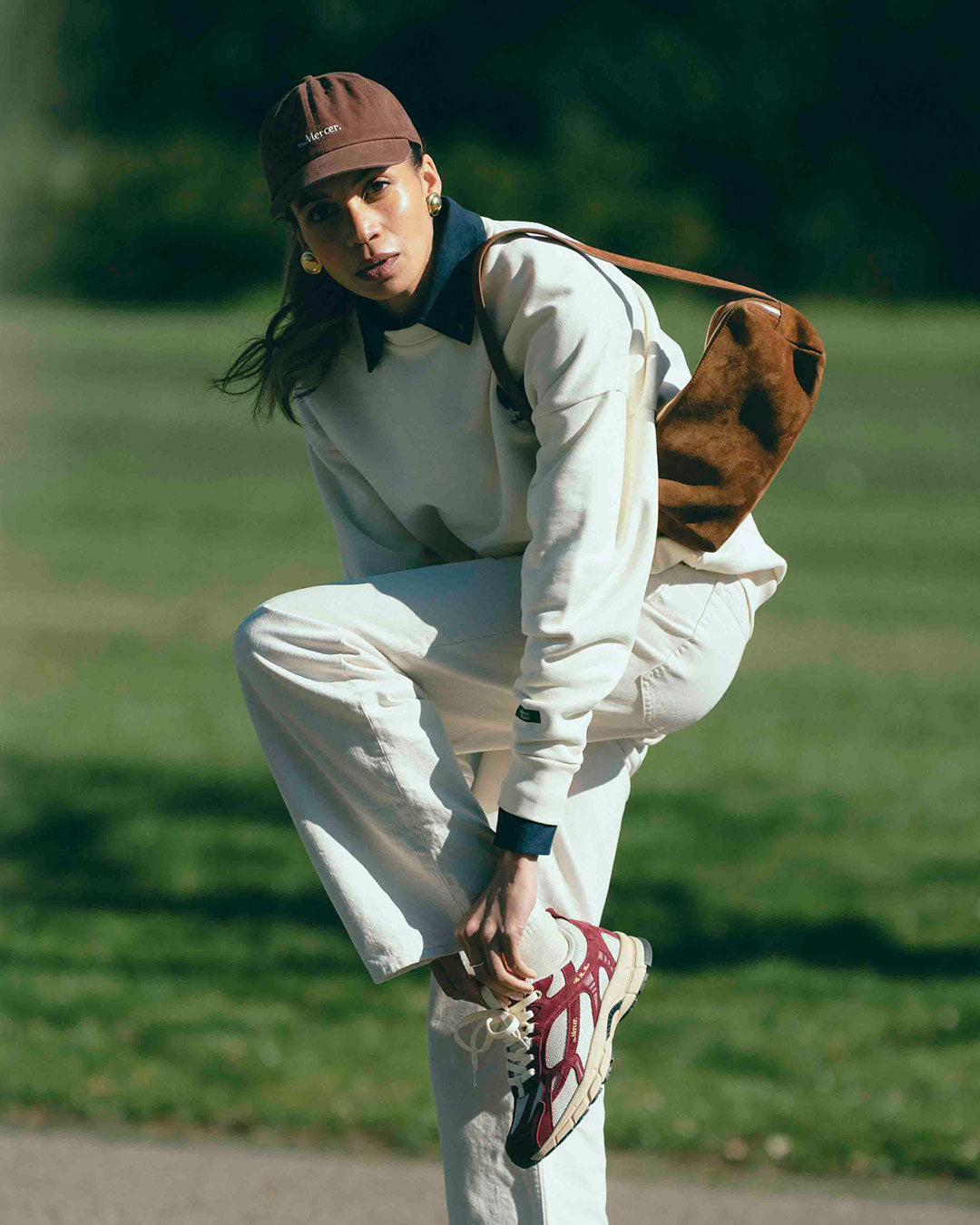 A woman is tying her The Re-Run Desert 2.0 in bordeaux. She is also wearing The Subway Sweater and The Mercer cap in brown.