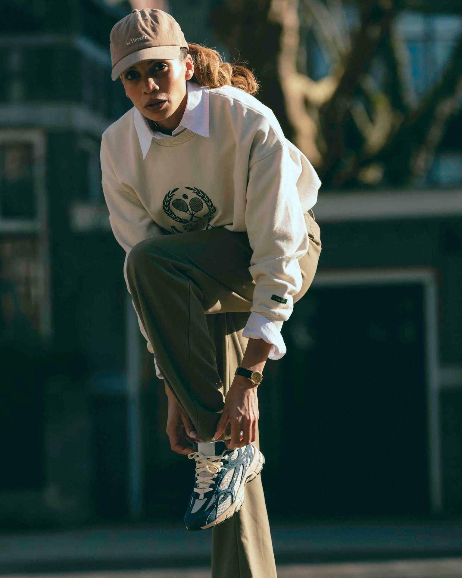 A woman is wearing The Re-Run Desert 2.0 in blue with The Mercer Tennis Sweater and The Mercer cap.