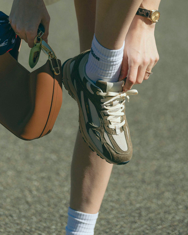 A woman is putting the tongue of The Re-Run Desert 2.0 in brown in the right way. She is also wearing matching Mercer socks.
