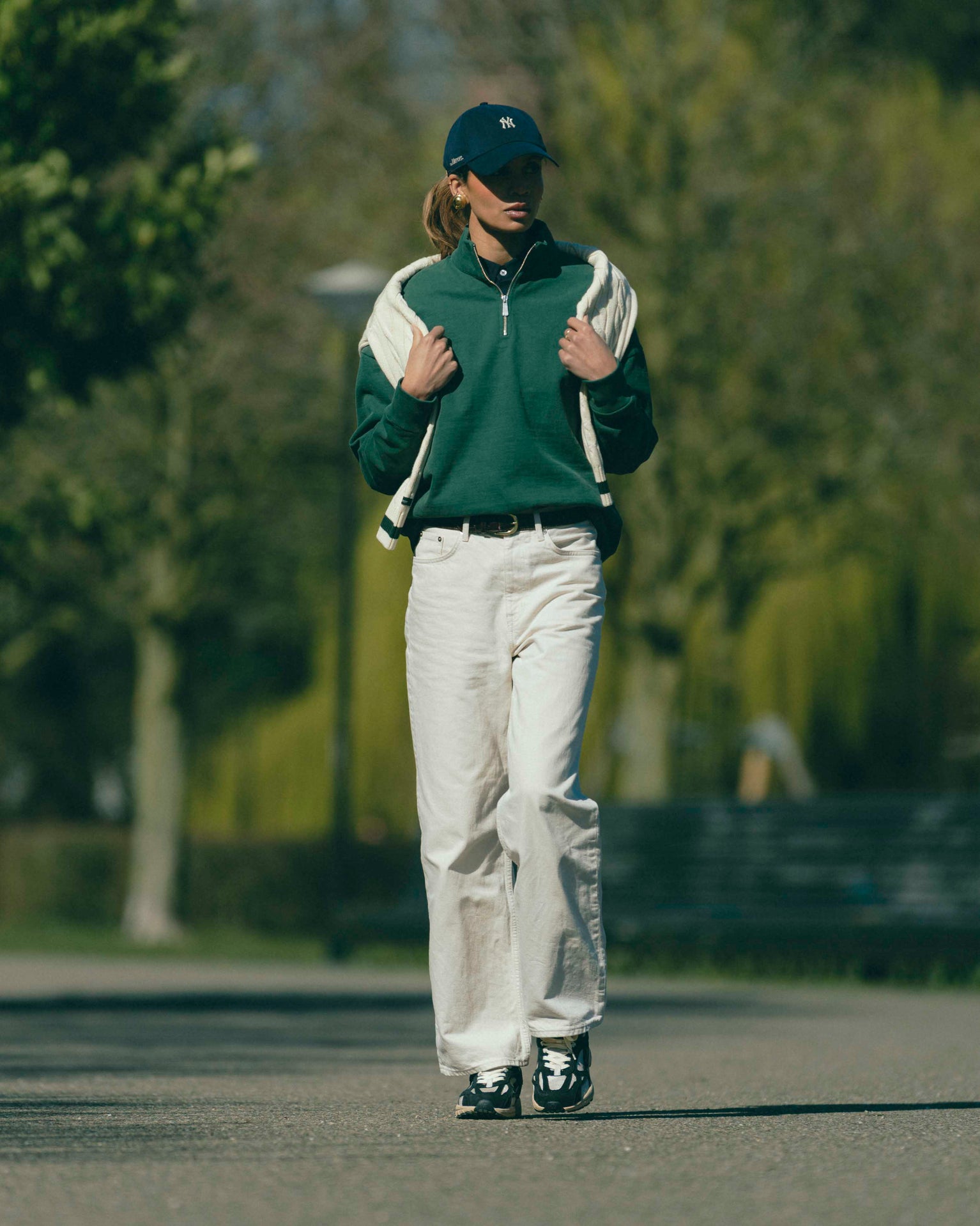 A woman is wearing The Mercer Tennis Quarterzip with The Mercer 47 cap. The shoes she is wearing are The RE-Run Desert 2.0 in antracite.