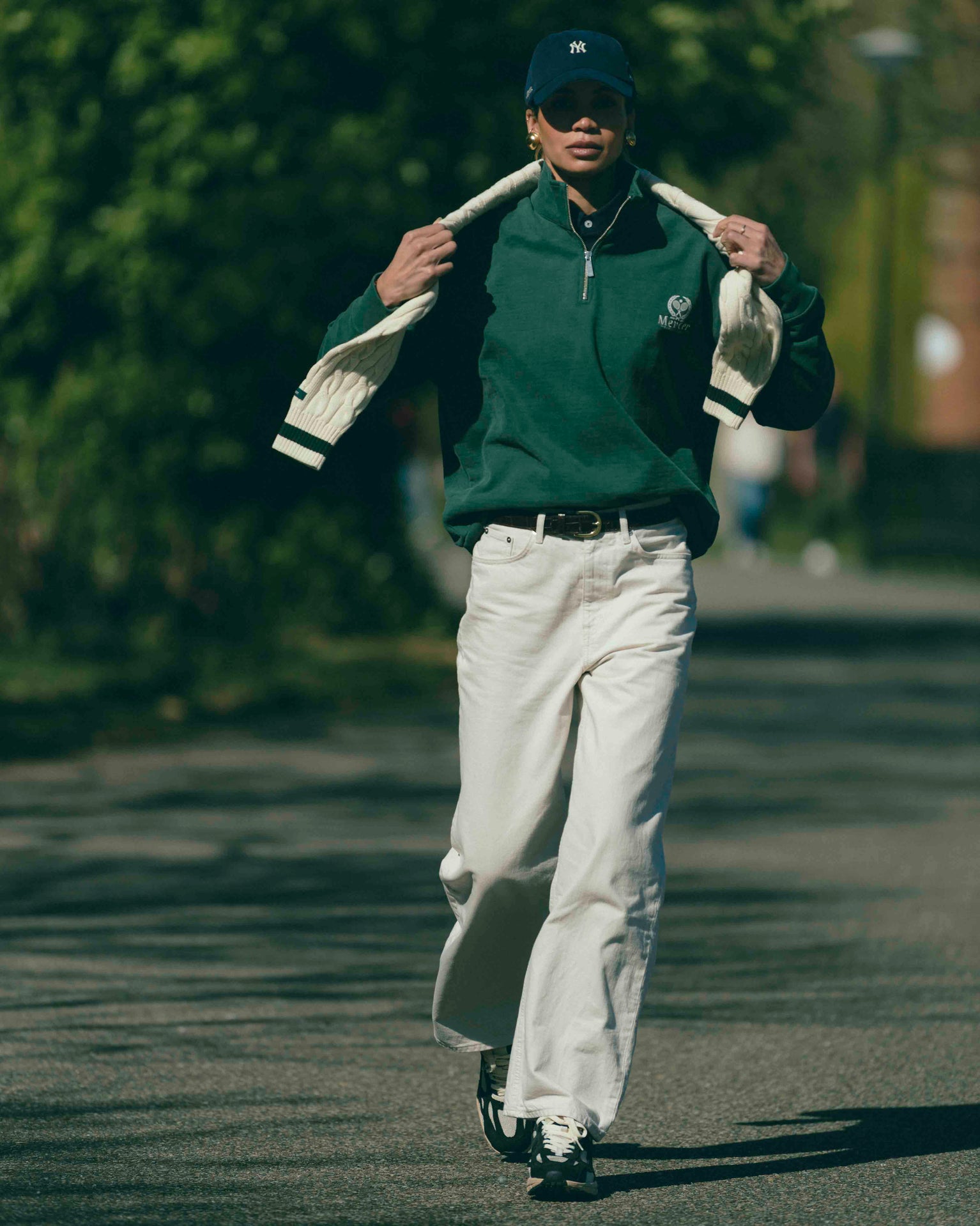 A woman is wearing The Mercer Tennis Quarterzip with The Mercer 47 cap. The shoes she is wearing are The RE-Run Desert 2.0 in antracite.