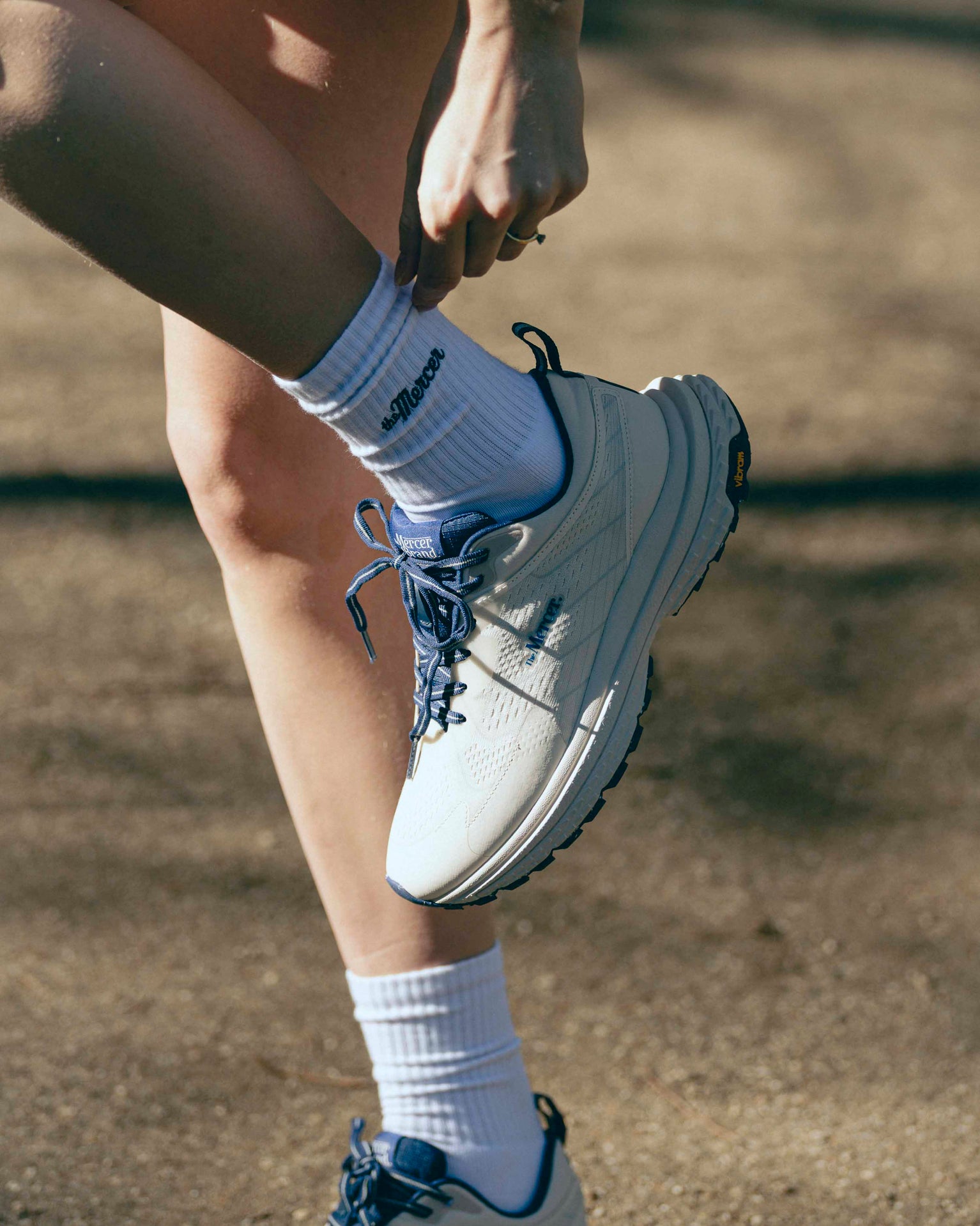A close up of a woman pulling her sock who is matching her The Mercer P22 in white/blue.