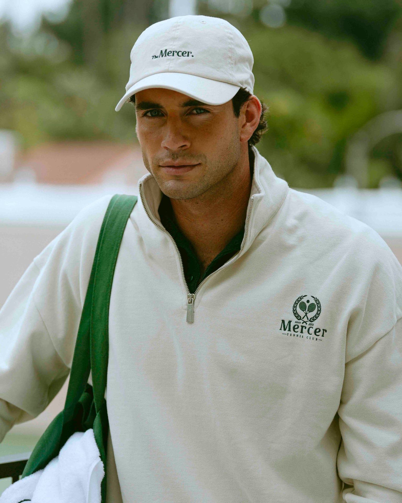 A man wearing The Mercer Tennis Cap in off white and matching Tennis Quarter zip.