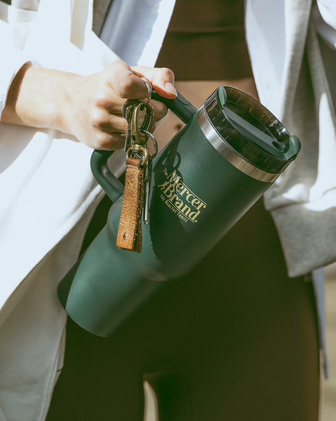 The Mercer Brand green tumbler with logo on light grey background